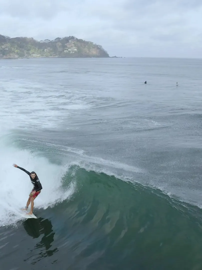 Drone view of a surfer riding along a breaking wave
